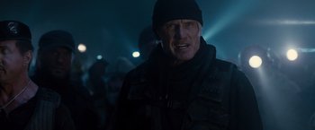 Movie still from “The Expendables 2” (2012), directed by Simon West – A man in a black jacket and a black hat is in the dark; Close Up shot, Low angle