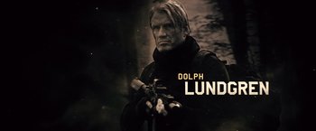 Movie still from “The Expendables 2” (2012), directed by Simon West – Dolph lundgren in a black outfit holding a gun; Medium shot, Low angle