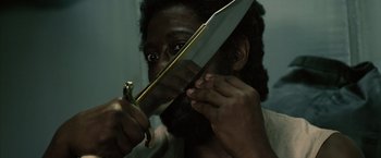 Movie still from “The Expendables 3” (2014), directed by Patrick Hughes – A bearded man holding a knife in front of his face; Close Up shot, High angle