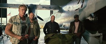Movie still from “The Expendables 3” (2014), directed by Patrick Hughes – A group of men standing next to each other in front of an airplane; Medium shot, Low angle