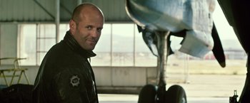 Movie still from “The Expendables 3” (2014), directed by Patrick Hughes – A man in a black jacket standing in front of an airplane; Close Up shot, Over the shoulder angle