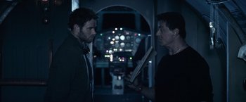 Movie still from “The Expendables 3” (2014), directed by Patrick Hughes – Two men are talking in front of an airplane cockpit at night; Medium shot, Over the shoulder angle