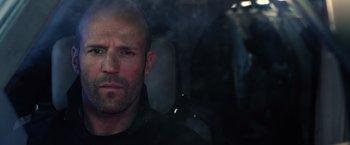 Movie still from “The Expendables 3” (2014), directed by Patrick Hughes – A man with a bald head sitting in a car; Close Up shot, Over the shoulder angle