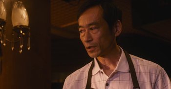 Movie still from “The Forest of Love” (2019), directed by Sion Sono – A man wearing an apron looking at the camera; Close Up shot, Low angle