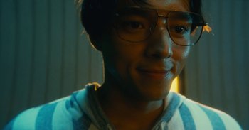 Movie still from “The Forest of Love” (2019), directed by Sion Sono – A person wearing glasses and smiling; Close Up shot, Low angle