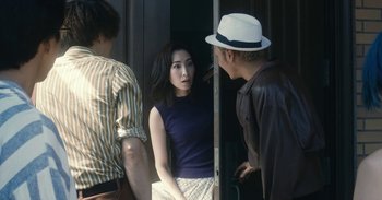 Movie still from “The Forest of Love” (2019), directed by Sion Sono – A man and a woman standing next to each other in front of another man; Medium shot, Over the shoulder angle