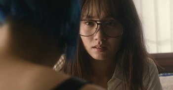 Movie still from “The Forest of Love” (2019), directed by Sion Sono – A woman with glasses looking at the camera; Close Up shot, Over the shoulder angle
