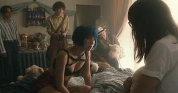 Movie still from “The Forest of Love” (2019), directed by Sion Sono – A woman sitting on top of a bed next to two men; Medium shot, Over the shoulder angle