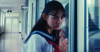 Movie still from “The Forest of Love” (2019), directed by Sion Sono – A young woman standing in front of a window; Close Up shot, Over the shoulder angle