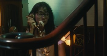 Movie still from “The Forest of Love” (2019), directed by Sion Sono – A woman is talking on a phone while sitting on a chair; Close Up shot, Low angle