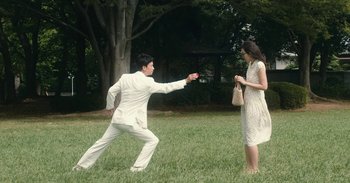 Movie still from “The Forest of Love” (2019), directed by Sion Sono – A man and a woman are playing a game in the grass; Wide shot, High angle