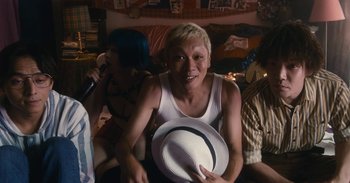 Movie still from “The Forest of Love” (2019), directed by Sion Sono – A man holding a white hat in front of a crowd; Medium shot, Low angle