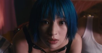 Movie still from “The Forest of Love” (2019), directed by Sion Sono – A woman with blue hair is looking at the camera; Close Up shot, Overhead angle