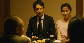 Movie still from “The Forest of Love” (2019), directed by Sion Sono – A man and a woman sitting at a dinner table; Medium shot, Over the shoulder angle