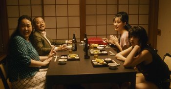 Movie still from “The Forest of Love” (2019), directed by Sion Sono – A group of people sitting at a table with plates of food; Medium shot, High angle