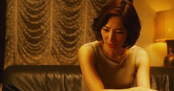 Movie still from “The Forest of Love” (2019), directed by Sion Sono – A woman sitting on top of a couch looking down; Close Up shot, Low angle