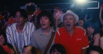 Movie still from “The Forest of Love” (2019), directed by Sion Sono – A group of people that are standing in a room; Medium shot, Low angle