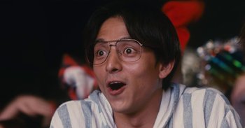 Movie still from “The Forest of Love” (2019), directed by Sion Sono – A person wearing glasses and looking surprised; Close Up shot, Low angle