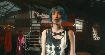 Movie still from “The Forest of Love” (2019), directed by Sion Sono – A woman with blue hair is posing for a picture; Close Up shot, Low angle