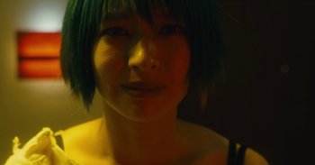 Movie still from “The Forest of Love” (2019), directed by Sion Sono – A person with green hair; Close Up shot, High angle