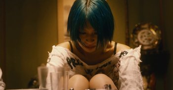 Movie still from “The Forest of Love” (2019), directed by Sion Sono – A woman with blue hair sitting on the floor; Close Up shot, Overhead angle