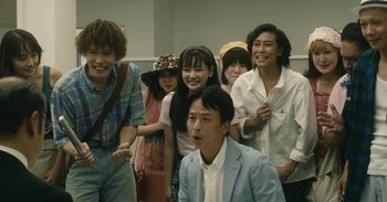 Movie still from “The Forest of Love” (2019), directed by Sion Sono – A group of people standing next to each other in a room; Medium shot, Low angle