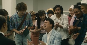 Movie still from “The Forest of Love” (2019), directed by Sion Sono – A group of people standing next to each other laughing; Medium shot, Low angle