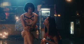 Movie still from “The Forest of Love” (2019), directed by Sion Sono – Two women sitting on a chair in a room; Medium shot, Low angle