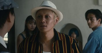 Movie still from “The Forest of Love” (2019), directed by Sion Sono – A man wearing a white hat and a striped shirt; Close Up shot, Low angle