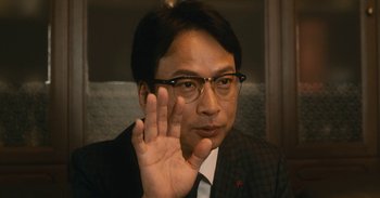 Movie still from “The Forest of Love” (2019), directed by Sion Sono – A man in a suit and tie holding his hand up; Close Up shot, Low angle