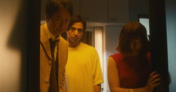 Movie still from “The Forest of Love” (2019), directed by Sion Sono – A group of people standing in a room; Medium shot, Low angle