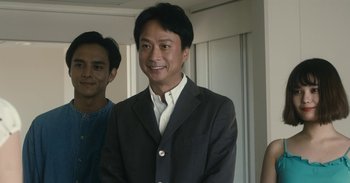 Movie still from “The Forest of Love” (2019), directed by Sion Sono – A man standing next to another man wearing a suit; Medium shot, Over the shoulder angle