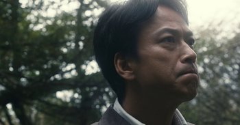 Movie still from “The Forest of Love” (2019), directed by Sion Sono – A person with a tree in the background; Close Up shot, Low angle