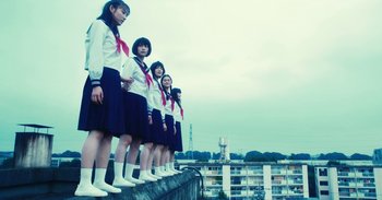 Movie still from “The Forest of Love” (2019), directed by Sion Sono – A group of young women standing on top of a building; Wide shot, Low angle