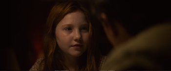 Movie still from “The Glass Castle” (2017), directed by Destin Daniel Cretton – A young girl looking at the camera in a dimly - lit room; Close Up shot, Over the shoulder angle