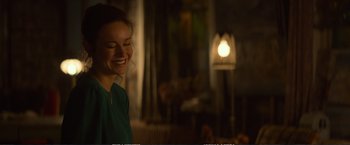 Movie still from “The Glass Castle” (2017), directed by Destin Daniel Cretton – A woman smiles brightly while standing next to a lamp; Close Up shot, Over the shoulder angle