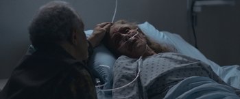 Movie still from “The Good Nurse” (2022), directed by Tobias Lindholm – An older woman laying in a hospital bed with an older man looking at her; Close Up shot, Over the shoulder angle