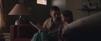 Movie still from “The Good Nurse” (2022), directed by Tobias Lindholm – A man sitting next to a little girl holding papers; Medium shot, Over the shoulder angle