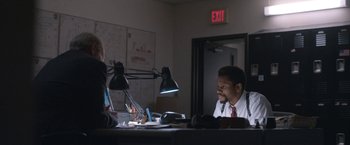 Movie still from “The Good Nurse” (2022), directed by Tobias Lindholm – A man sitting at a desk in front of another man; Medium shot, Over the shoulder angle