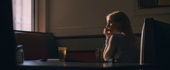 Movie still from “The Good Nurse” (2022), directed by Tobias Lindholm – A woman sitting at a table with a glass of water; Medium shot, Over the shoulder angle