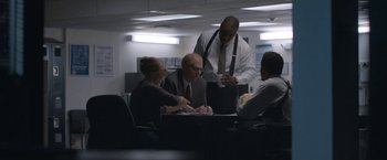 Movie still from “The Good Nurse” (2022), directed by Tobias Lindholm – A group of people sitting around a table in an office; Medium shot, Over the shoulder angle