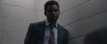 Movie still from “The Good Nurse” (2022), directed by Tobias Lindholm – A man wearing a suit and tie standing in front of a brick wall; Medium shot, Low angle