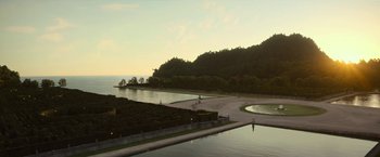 Movie still from “The Gray Man” (2022), directed by Joe Russo – A man riding a bike on top of a road next to a lake; Extreme Wide shot, High angle