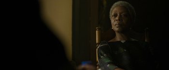 Movie still from “The Gray Man” (2022), directed by Joe Russo – An older woman sitting at a table with a cell phone in front of her; Close Up shot, Over the shoulder angle