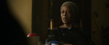 Movie still from “The Gray Man” (2022), directed by Joe Russo – An older woman sitting at a table with a beer; Close Up shot, Over the shoulder angle