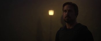 Movie still from “The Gray Man” (2022), directed by Joe Russo – A man standing in the dark with a light behind him; Close Up shot, Over the shoulder angle