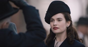 Movie still from “The Guernsey Literary and Potato Peel Pie Society” (2018), directed by Mike Newell – A woman wearing a black hat with a bow on her head; Close Up shot, Over the shoulder angle