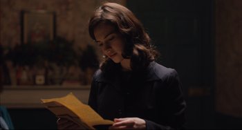 Movie still from “The Guernsey Literary and Potato Peel Pie Society” (2018), directed by Mike Newell – A woman in a dark room looking down at a piece of paper; Close Up shot, Over the shoulder angle