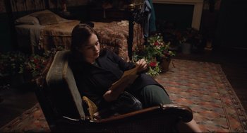 Movie still from “The Guernsey Literary and Potato Peel Pie Society” (2018), directed by Mike Newell – A woman sitting in a chair looking at a piece of paper; Medium shot, High angle