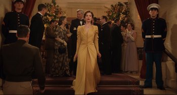 Movie still from “The Guernsey Literary and Potato Peel Pie Society” (2018), directed by Mike Newell – A woman in a yellow dress walking down the stairs; Wide shot, Low angle